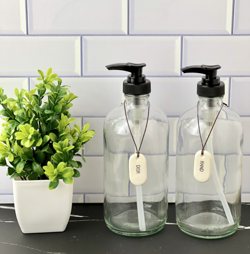 Two clear glass bottles with pump tops next to a small green plant