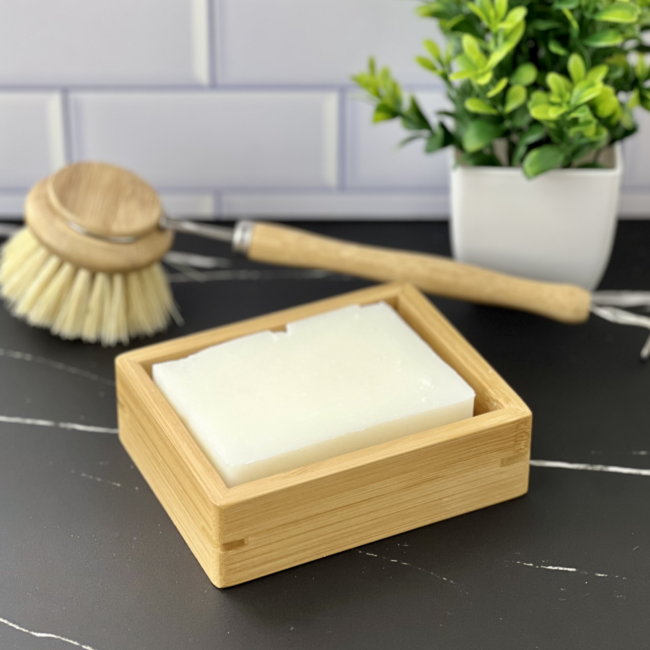 bamboo soap shelf in the foreground with a bamboo dish brush and small plant in the background