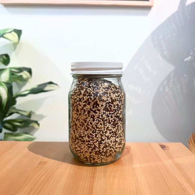 A clear mason jar filled with tri-color quinoa sitting on a wooden table