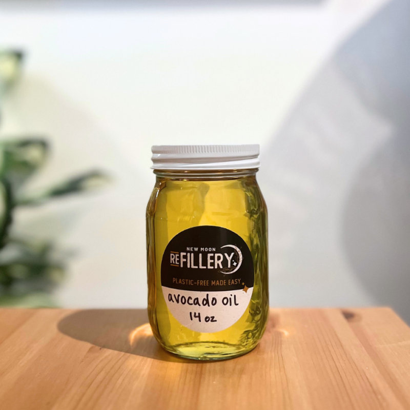 A clear glass jar filled with avocado oil sitting on a wooden table